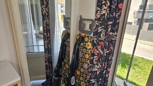 A room with a large mirror, a vacuum cleaner, floral curtains, and a view of the outside. - Casa Carmel (Kamen)