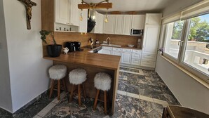 A modern kitchen with a wooden island, bar stools, a hanging light fixture, and a view through a window. - Casa Carmel (Kamen)
