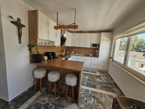 Eine moderne Küche mit einer Holzinsel, Barhocker, einer Pendelleuchte und Blick durch ein Fenster.
