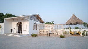 A white building with a thatched-roof structure, outdoor seating, and a clear sky. - Mahika Valley Stay (Jaipur)