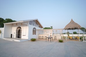 A white building with a thatched-roof structure, outdoor seating, and a clear sky. - Mahika Valley Stay (Jaipur)