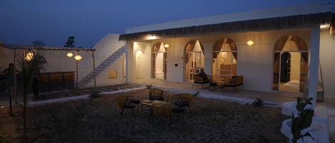 A building with a covered outdoor seating area, a staircase leading to an upper level, and a sandy courtyard.