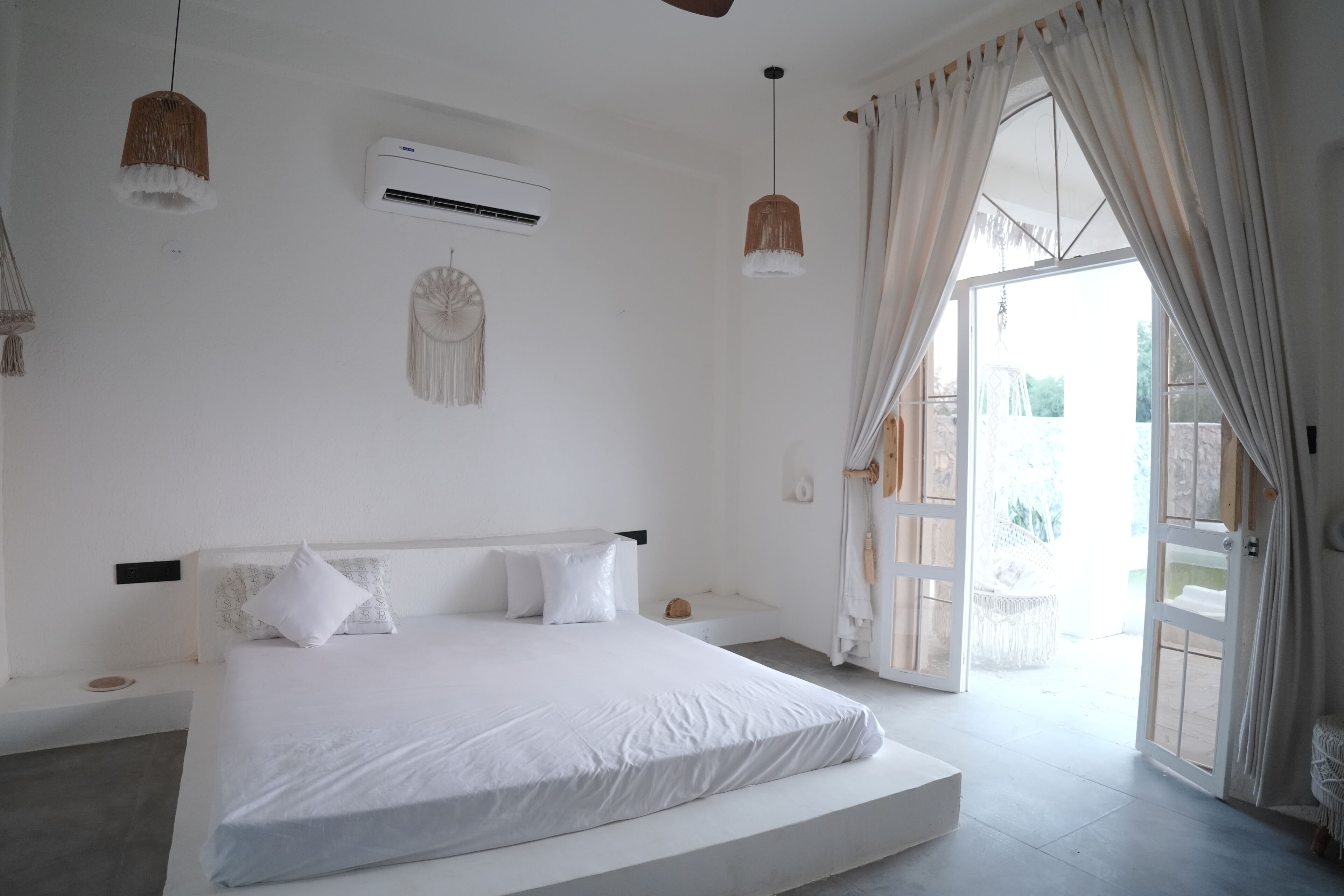 A bedroom with a bed, an air conditioning unit, a wall hanging, and a view through a door.