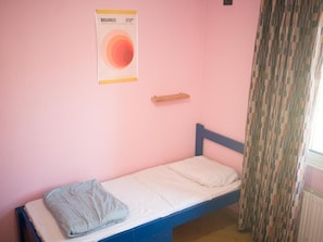 Una cama individual con cabecera azul en una habitación con paredes rosas.