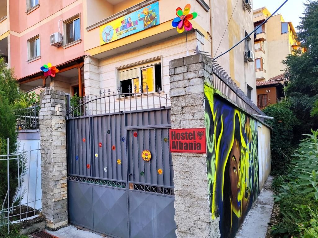 Ostello con un cartello colorato, un ingresso chiuso da cancello e un murale sulla parete.