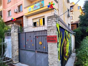 Ostello con un cartello colorato, un ingresso chiuso da cancello e un murale sulla parete.