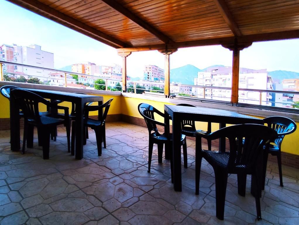 Una terrazza esterna con tetto in legno, piastrelle esagonali e tavoli e sedie in plastica nera.
