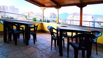 Una terrazza esterna con tetto in legno, piastrelle esagonali e tavoli e sedie in plastica nera.