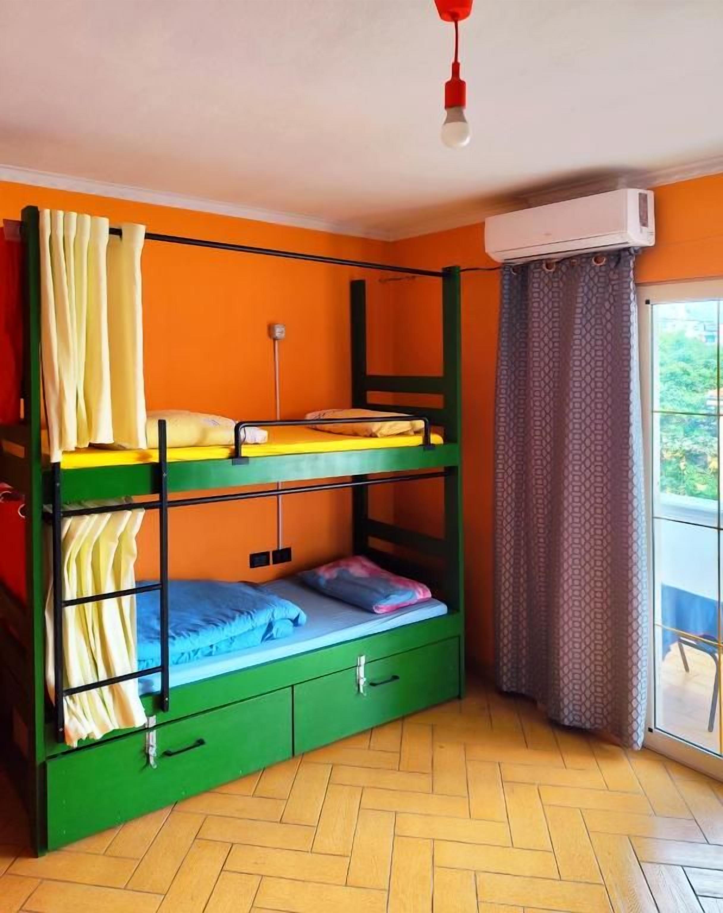 Un letto a castello con struttura verde, una piccola scrivania e una finestra con tende.
