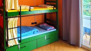 Uma cama beliche com estrutura verde, uma escrivaninha pequena e uma janela com cortinas.