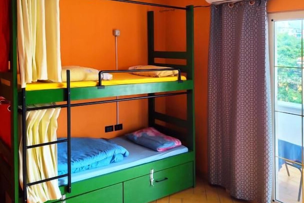 Un letto a castello con struttura verde, una piccola scrivania e una finestra con tende.