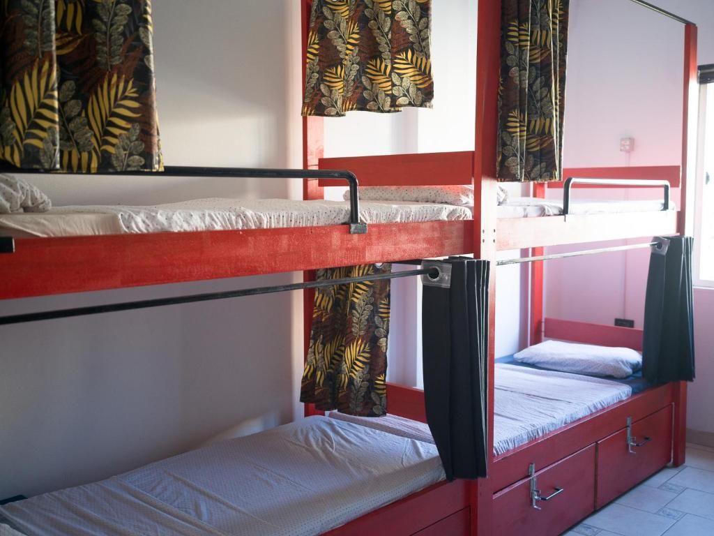 Een slaapkamer met stapelbed, een rood frame, een onderste bed met een witte matras en een bovenste bed met een zwarte matras.