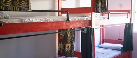 Une chambre avec un lit superposé, dont la structure est rouge, avec un lit inférieur doté d’un matelas blanc et un lit supérieur doté d’un matelas noir.