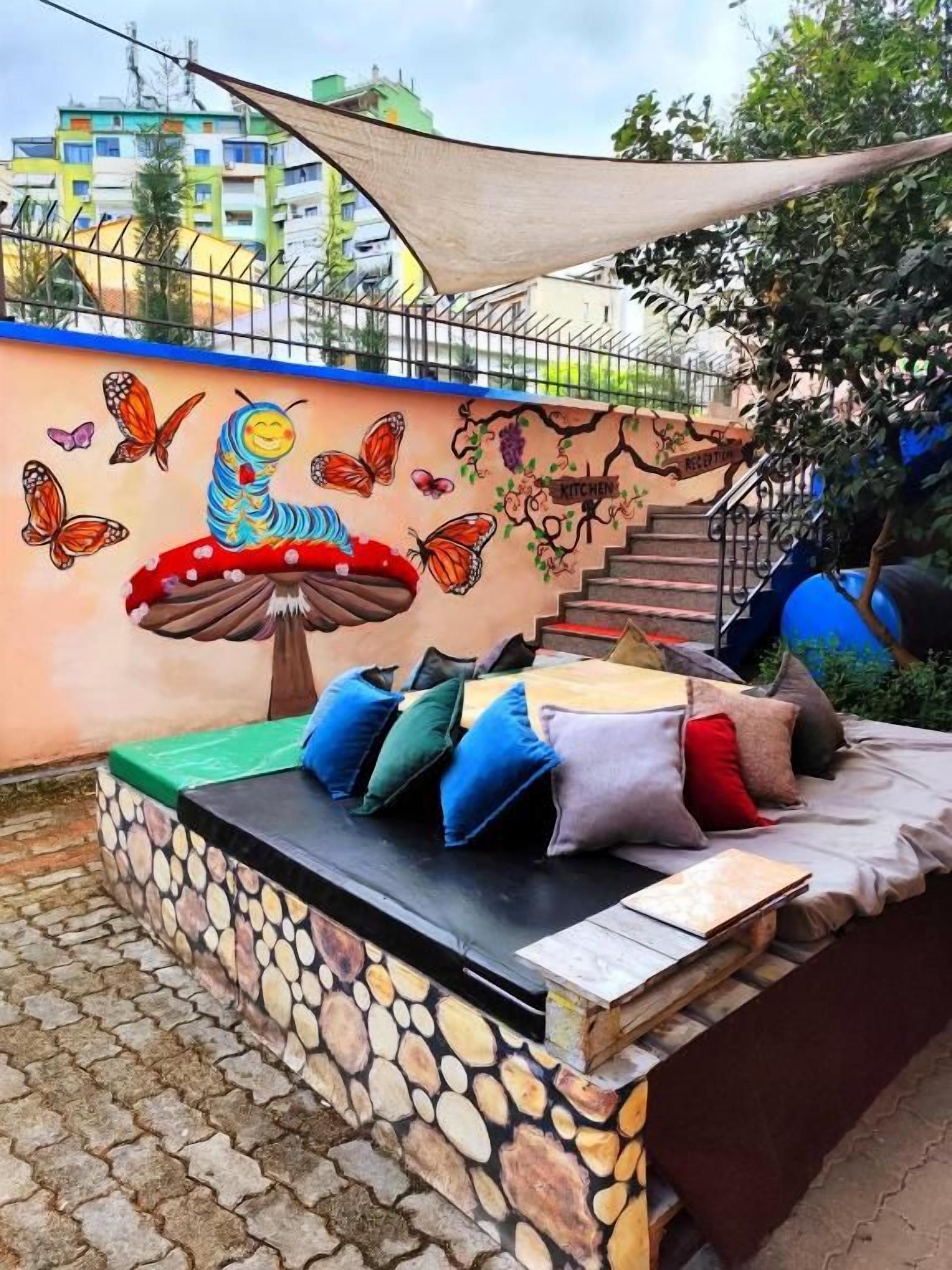 An outdoor seating area with a stone wall, colorful mural, and a staircase.