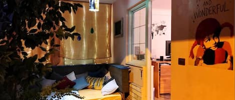 A cozy room with a bed, a hanging light fixture, and a wall with a character illustration.