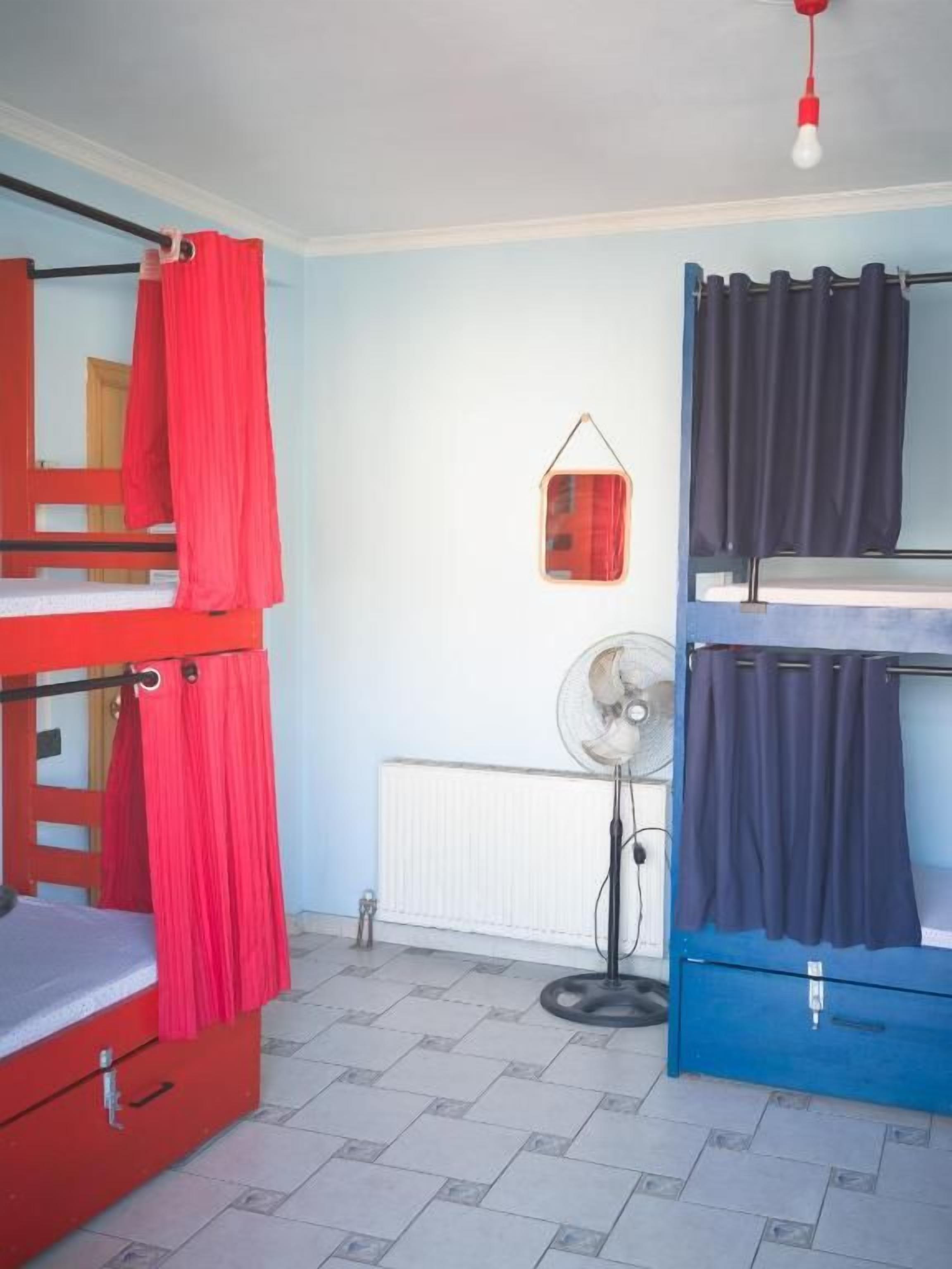 A dormitory room with bunk beds, a fan, and a radiator.