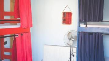 A dormitory room with bunk beds, a fan, and a radiator.