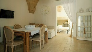 Uma área de refeições com mesa e cadeiras de madeira, toalha de mesa branca e teto com um design de pedra original.