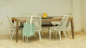Área de refeições à beira da piscina com mesa e cadeiras, luminária pendente e um detalhe decorativo na parede.