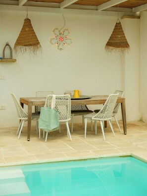 Ein Essbereich am Pool mit Tisch und Stühlen, einer Hängelampe und einer dekorativen Wandgestaltung.