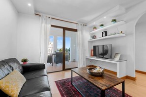 A modern living room with a leather sofa, a coffee table, and a TV on a white stand. There is a balcony with a view of buildings and a railing. - Sea Views Apartment with Terrace and Pools (Puerto de la Duquesa)