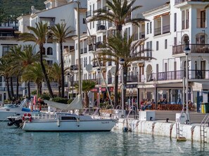 A marina with boats docked, palm trees, and a row of white buildings with balconies. - Sea Views Apartment with Terrace and Pools (Puerto de la Duquesa)
