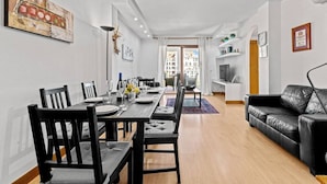 En moderne stue med et spiseområde, en sort lædersofa og et spisebord dækket til fire personer.