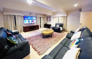 Una sala moderna con un televisor de pantalla plana grande, sofás oscuros, una mesa de centro y una alfombra estampada.