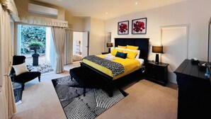 Une chambre spacieuse avec un grand lit, un coin salon avec un fauteuil et une vue sur un jardin, accessible par une porte coulissante.