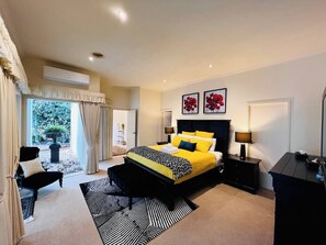 Une chambre spacieuse avec un grand lit, un coin salon avec un fauteuil et une vue sur un jardin, accessible par une porte coulissante.