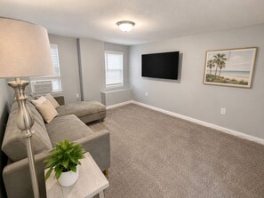 A living room with a grey sofa, a lamp, a flat-screen TV, and a framed picture on the wall. - Beach Casita 1-bedroom Apt by Boardwalk and Beach (Ocean City)
