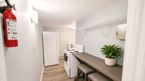 A compact kitchen with a white refrigerator, stove, and microwave. There is a fire extinguisher mounted on the wall and a potted plant on the counter. - Beach Casita 1-bedroom Apt by Boardwalk and Beach (Ocean City)