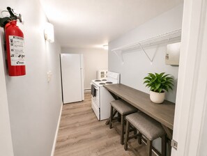 A compact kitchen with a white refrigerator, stove, and microwave. There is a fire extinguisher mounted on the wall and a potted plant on the counter. - Beach Casita 1-bedroom Apt by Boardwalk and Beach (Ocean City)