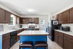 Una cocina con armarios de madera, una isla central, lavavajillas, horno, refrigerador y microondas.