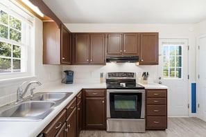 Una cocina con armarios de madera, un lavamanos de acero inoxidable, un horno empotrado y una ventana que proporciona luz natural.