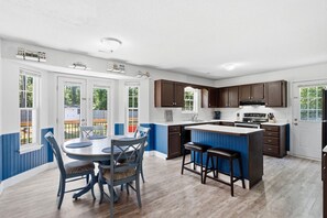 A modern kitchen with a central island, dark wooden cabinets, and a dining area with blue chairs.