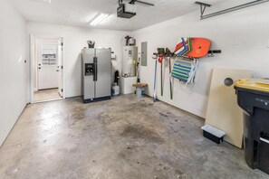 En garage med et stort køleskab, vandvarmer samt diverse værktøj og udstyr.