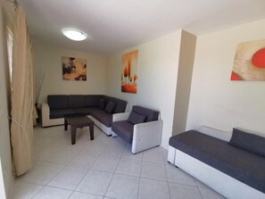 A living room with a sectional sofa, a small table, and two wall-mounted paintings. - Sidari Water Park Resort & Spa (Corfu)