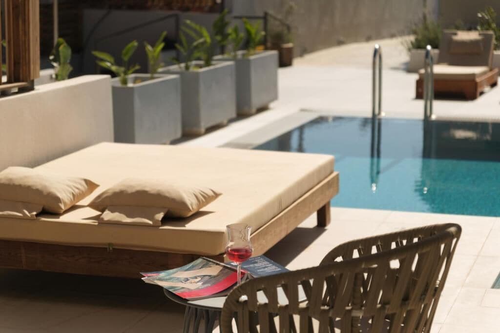 Un espace aménagé au bord de la piscine avec un lit, une chaise longue et une bouteille de vin rouge posée sur une table.