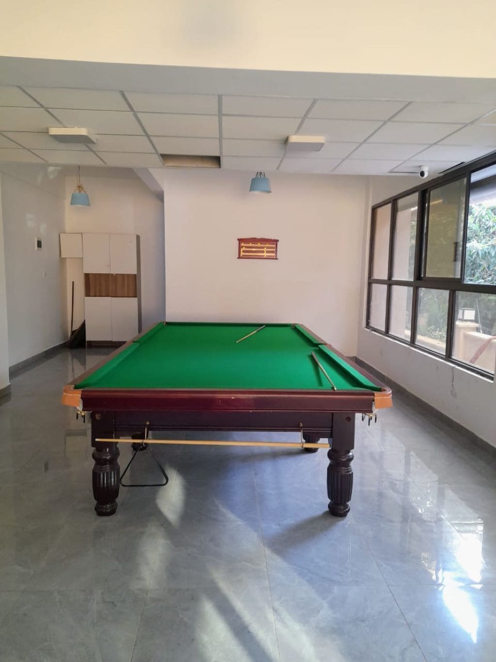 Uma mesa de bilhar em um espaço com janela, porta e um letreiro fixado na parede.