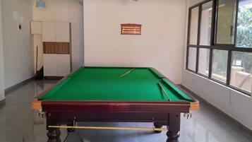 Uma mesa de bilhar em um espaço com janela, porta e um letreiro fixado na parede.