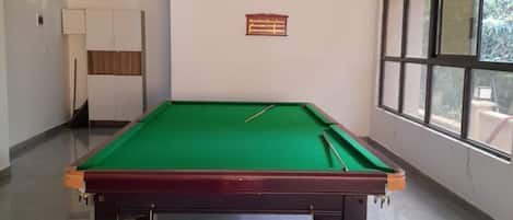 A pool table in a room with a window, a door, and a wall-mounted sign.