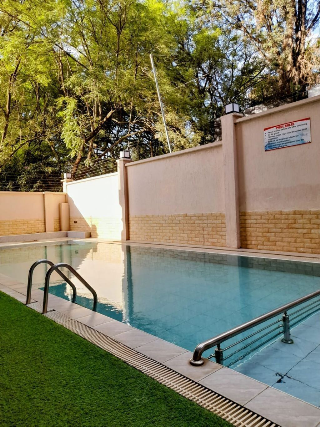A swimming pool with a safety sign, surrounded by a brick wall and greenery.