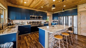 Une cuisine moderne avec des armoires bleues, des appareils en acier inoxydable, un îlot en marbre et un plancher en bois.