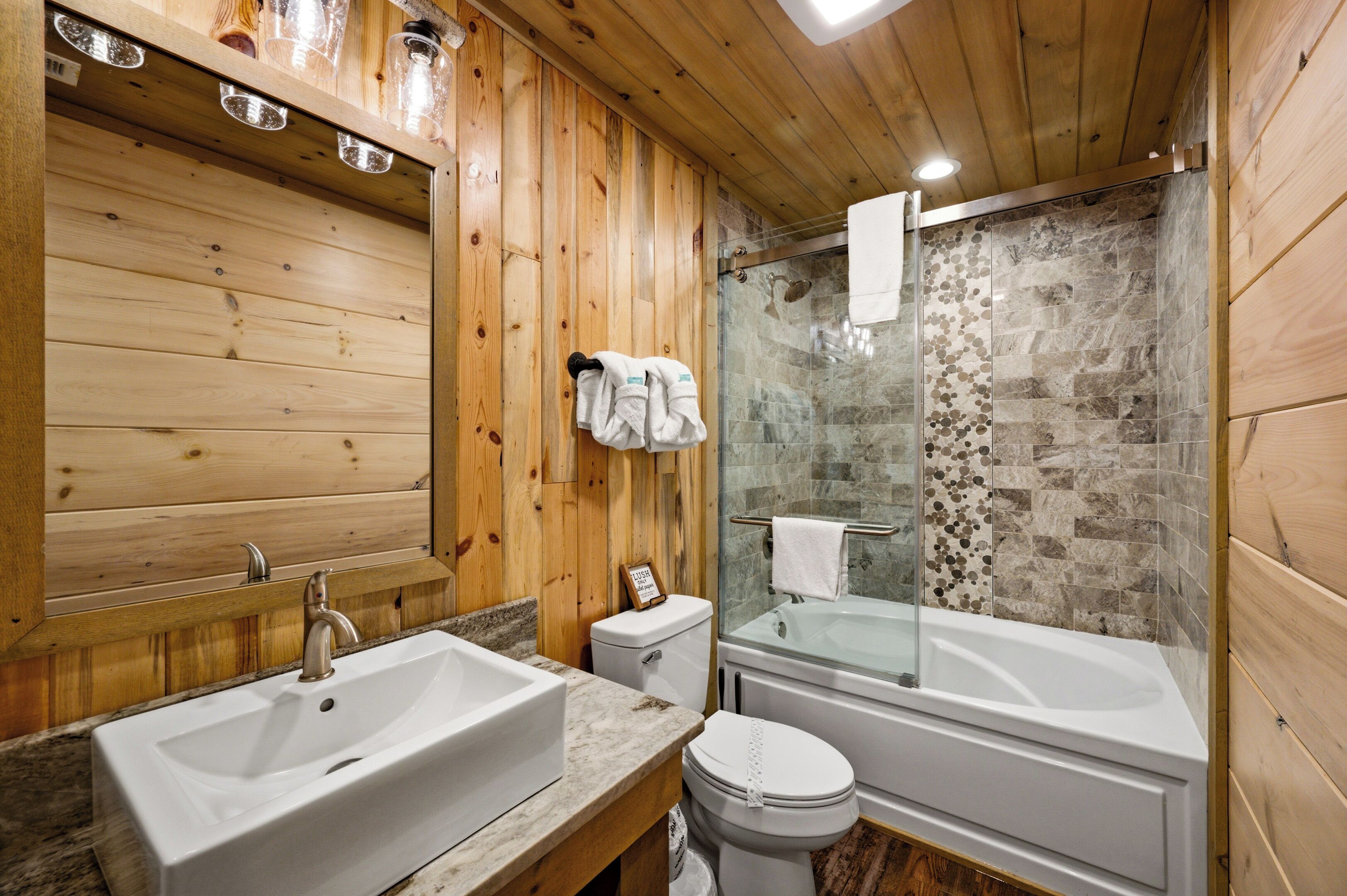Un bagno con rivestimento in legno, dotato di doppio lavabo, WC e cabina doccia in vetro.