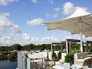 An outdoor seating area with umbrellas, tables, and chairs overlooking a body of water. - Tattershall Lakes Country Park - Holiday Accommodation 16605 (Lincoln)