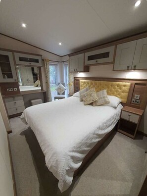 A bedroom with a large bed, a bedside table, a nightstand, a wardrobe, and a mirror. - Tattershall Lakes Country Park - Holiday Accommodation 16605 (Lincoln)