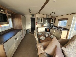 A compact kitchen with a dining area, including a microwave, cabinets, and a table set for four. - Tattershall Lakes Country Park - Holiday Accommodation 16605 (Lincoln)