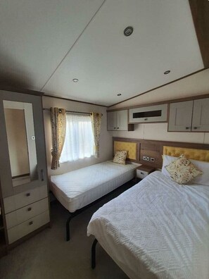 A compact hotel room with two single beds, a small desk, a mirror, and a window with curtains. - Tattershall Lakes Country Park - Holiday Accommodation 16605 (Lincoln)