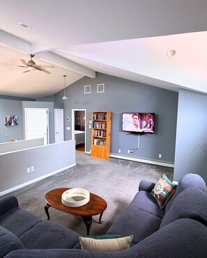 A living room with a grey sofa, a coffee table, a bookshelf, and a TV mounted on the wall. - Peaceful Canal-Front 1 bedroom Retreat Near Hospitals, LIRR & Beaches (Lindenhurst)
